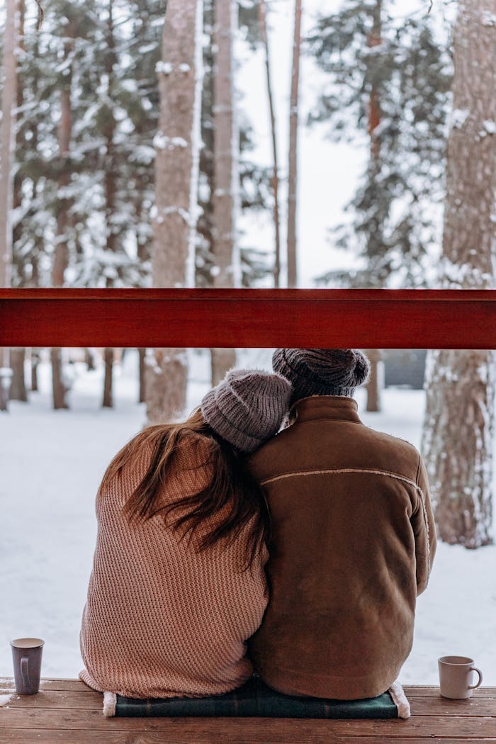 services-04 A couple in cozy winter attire sitting together in a snowy forest, enjoying a warm drink.