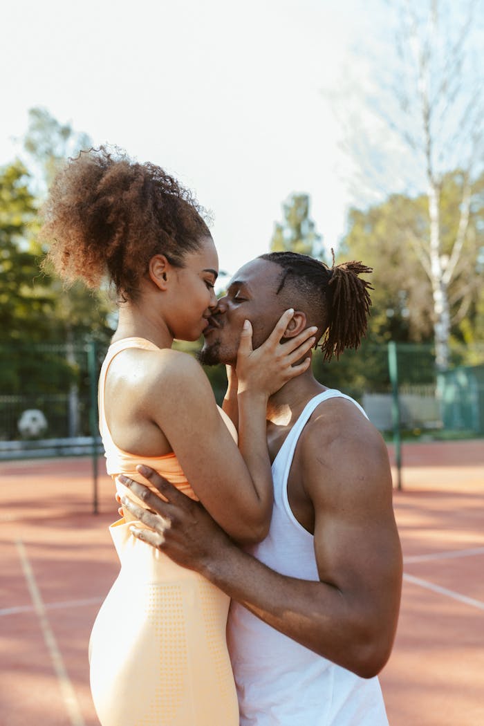 gallery-04 Loving couple sharing a kiss on a sunny tennis court. Outdoor romance.